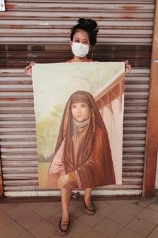 Woman wearing a face mask holding a portrait of a young girl dressed in traditional clothing.