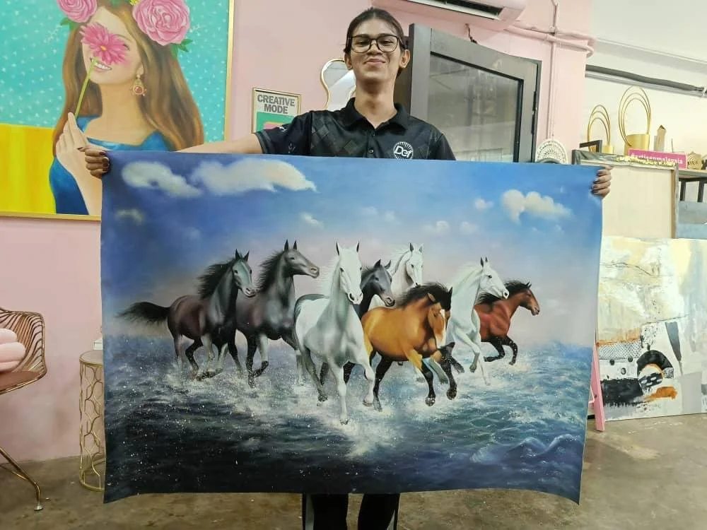 A woman holding a painting of eight horses running through water with a cloudy sky in the background.