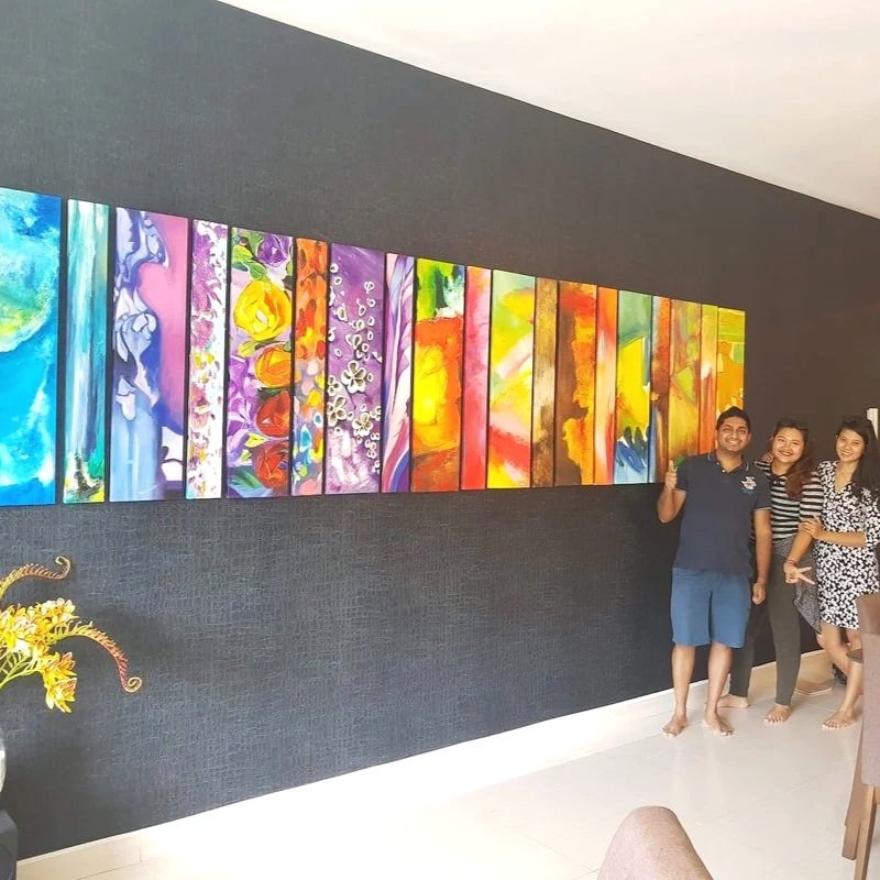 Three people standing in front of a colorful abstract painting on a black wall, with a small plant with yellow flowers in the foreground.