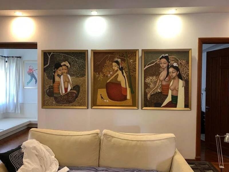Three framed artworks of women in traditional attire hanging on a living room wall above a light-colored sofa.