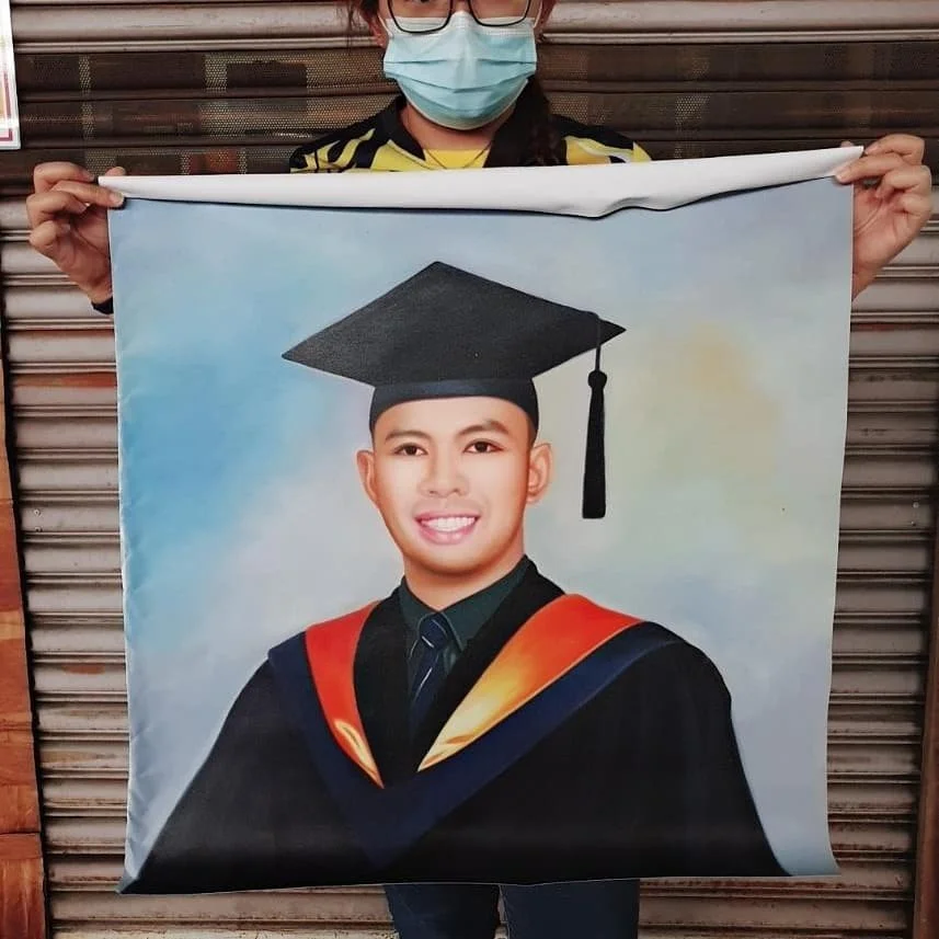 A person wearing glasses and a face mask holding a large banner with a portrait of a young man in a graduation cap and gown.