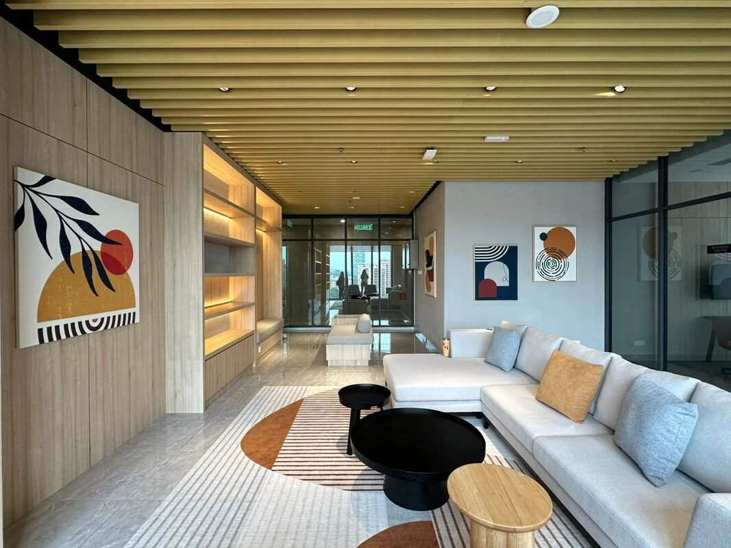 Modern hotel lobby with beige sectional sofa, colorful pillows, contemporary abstract paintings on the walls, wooden accents, and geometric patterned area rug.