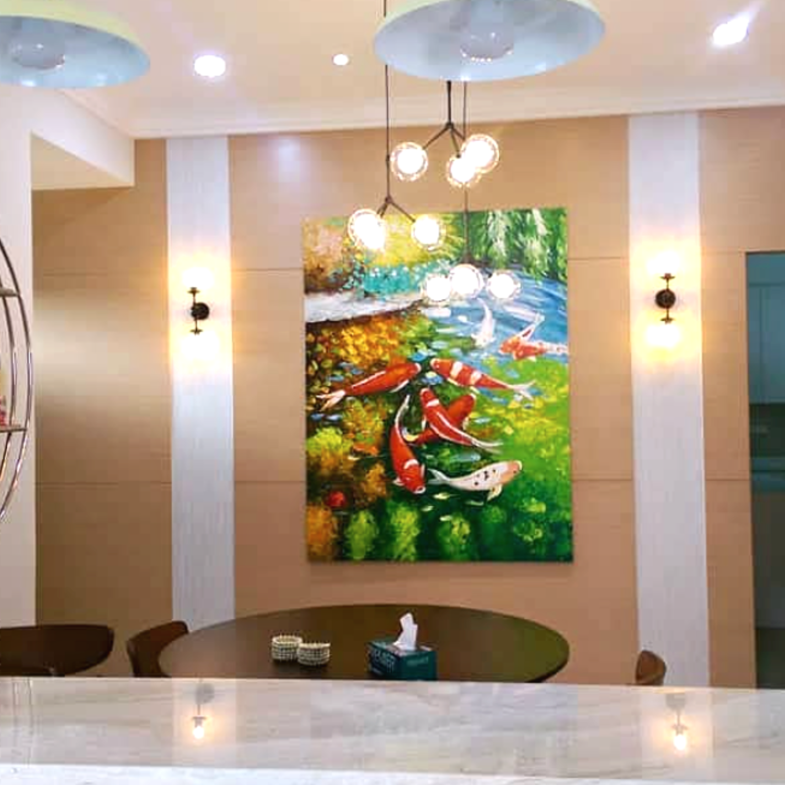 Interior of a room with a beige ceiling and wall, two wall-mounted lamps, a large colorful abstract painting, a chandelier with multiple round lights, and a dark wooden dining table with chairs.