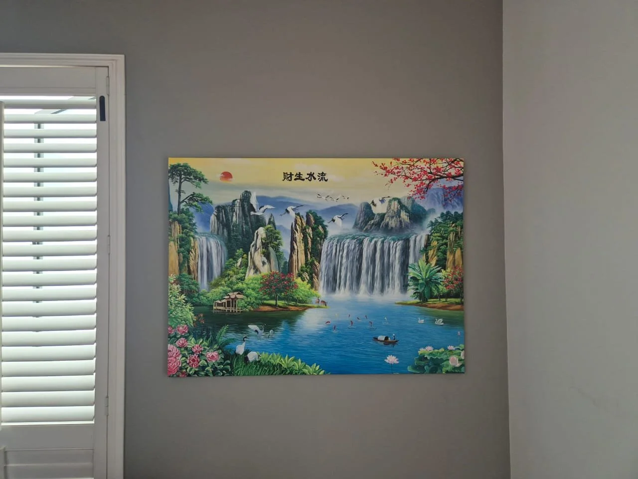 Colorful painting of a waterfall landscape with mountains, trees, water, and birds on a gray wall.