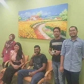 Group of five people posing in front of a colorful landscape painting on a lime green wall.