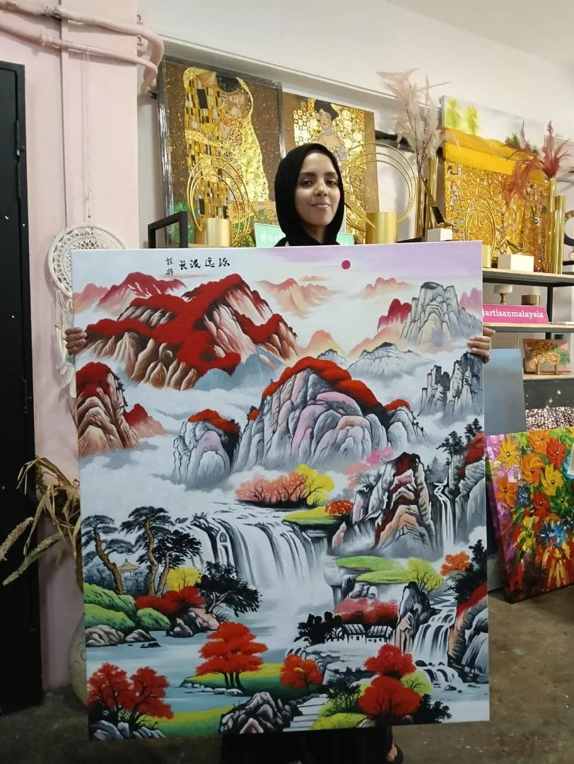 Woman in black headscarf holding large traditional Chinese-style landscape painting with mountains, waterfalls, trees, and a red sun.
