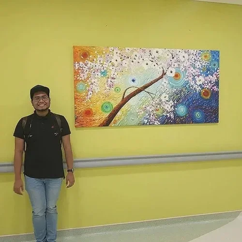 A person standing in front of a colorful abstract painting on a yellow wall.