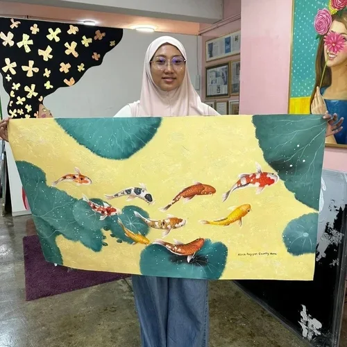 A woman wearing glasses and a hijab holds a painting of koi fish swimming in water with large green lily pads against a yellow background, in an indoor setting with decorated walls and framed awards or certificates.