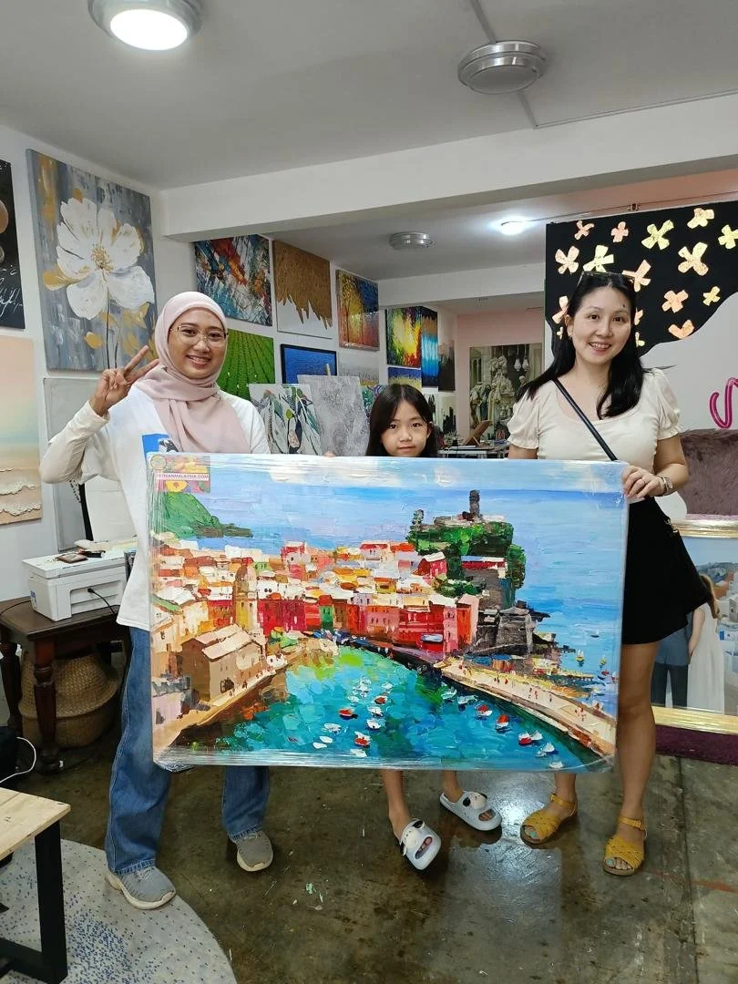 Three women and a girl holding a colorful, impressionistic painting of a city coastal scene with water, boats, and buildings, inside an art gallery with various artworks on the walls.