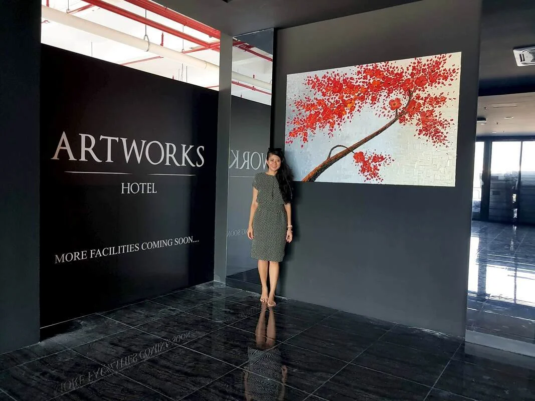 Woman in a checkered dress standing inside a hotel art gallery with a large red leaf painting on the wall.