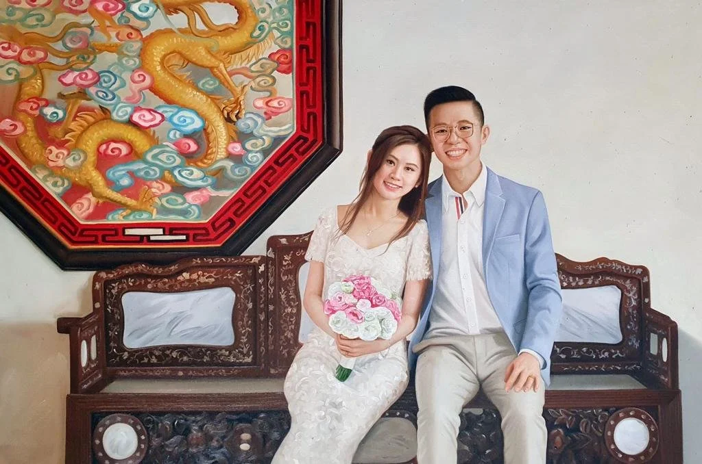 A smiling couple sitting on a carved wooden bench, with the woman holding a bouquet of pink and white flowers. Behind them is a traditional Chinese dragon artwork.