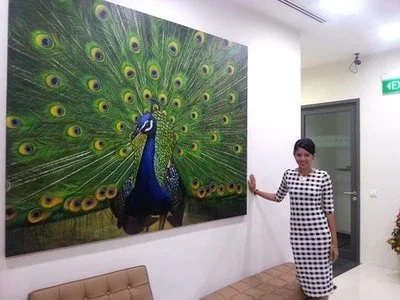 A woman in a black and white checkered dress standing in a room decorated with a large peacock painting on the wall.