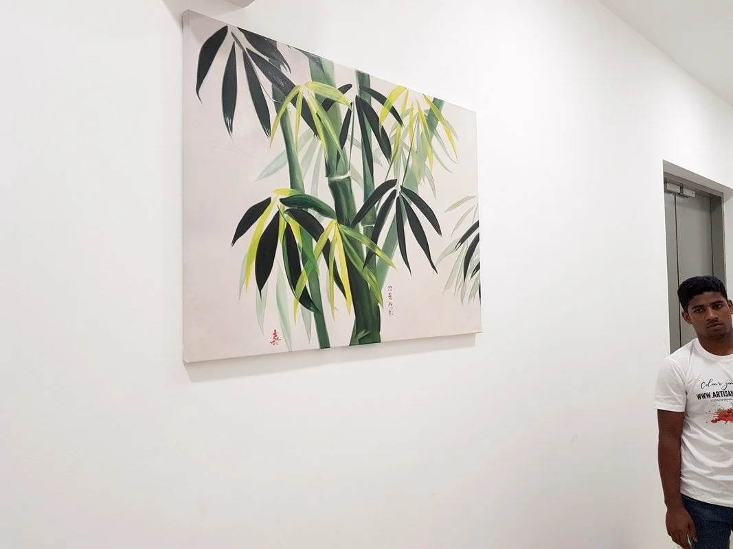 Painting of bamboo stalks and leaves on a white wall, with a young man standing to the right.