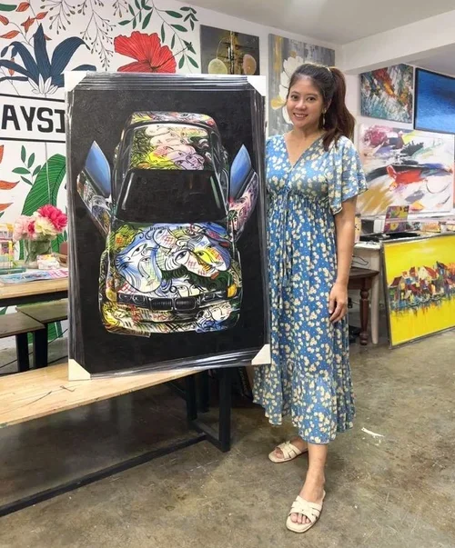 A woman in a blue floral dress standing beside a painting of a car with graffiti art on it, displayed on an easel inside an art gallery.