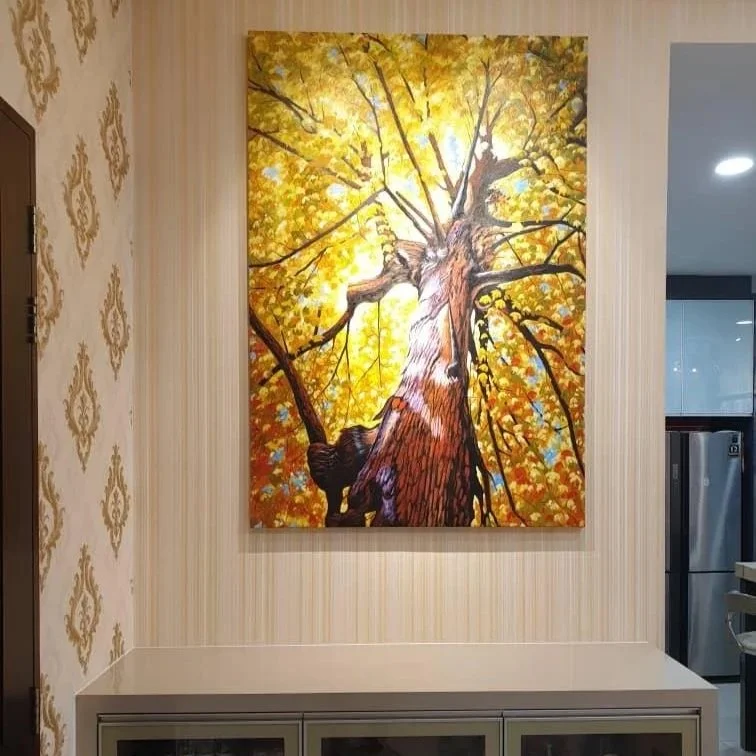Painting of a tree with yellow leaves viewed from below, with sunlight filtering through the branches, mounted on a wall inside a home or building.