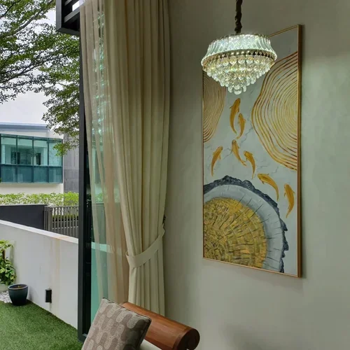 Interior view of a living space with a chandelier, a painting of koi fish and a tree outside visible through a large glass window.