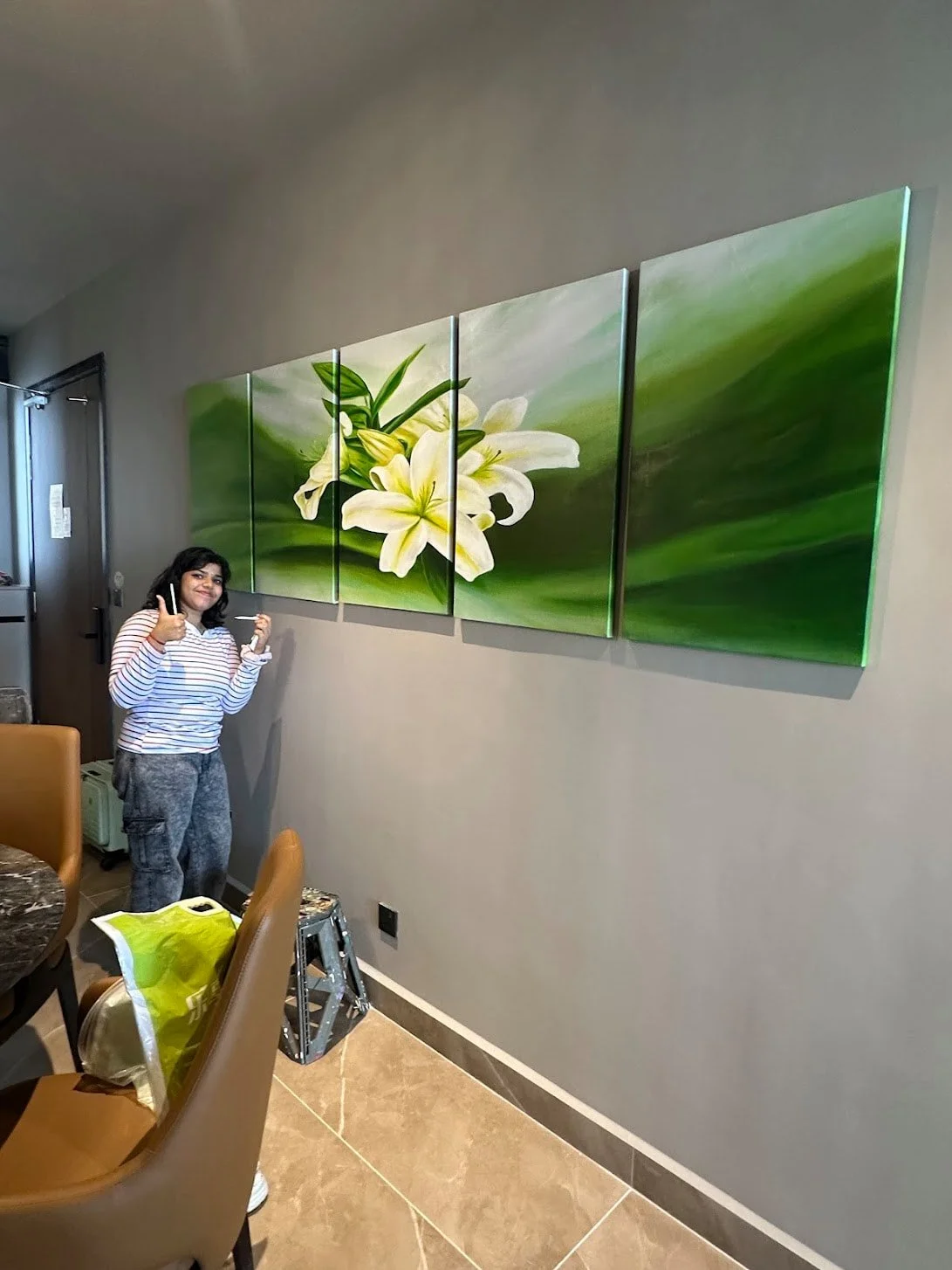 A woman standing next to a four-panel wall art piece featuring white lilies and green leaves, giving a thumbs-up and smiling.
