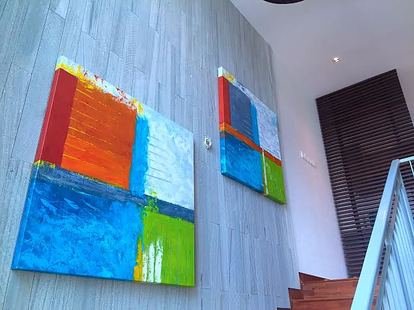 Two abstract paintings with colorful blocks on a light gray wooden wall.