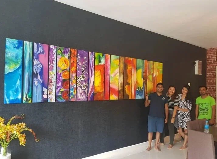 Four people standing in front of a colorful abstract painting on a dark wall in a room with gray and brick decor.