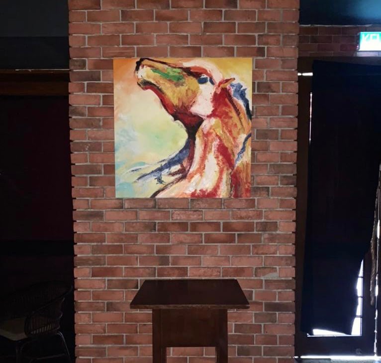 Abstract colorful painting of a dog hanging on a brick wall above a small wooden table.
