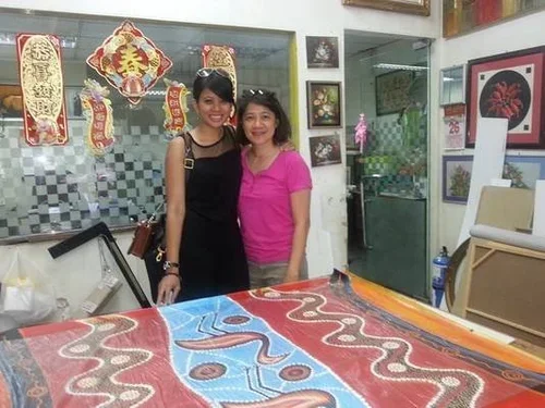 Two women stand behind a large snake-themed fabric or artwork inside a decorated room.