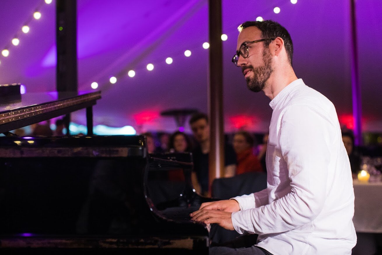 Un homme jouant du piano lors d'un événement dans une tente décorée avec des lumières colorées.