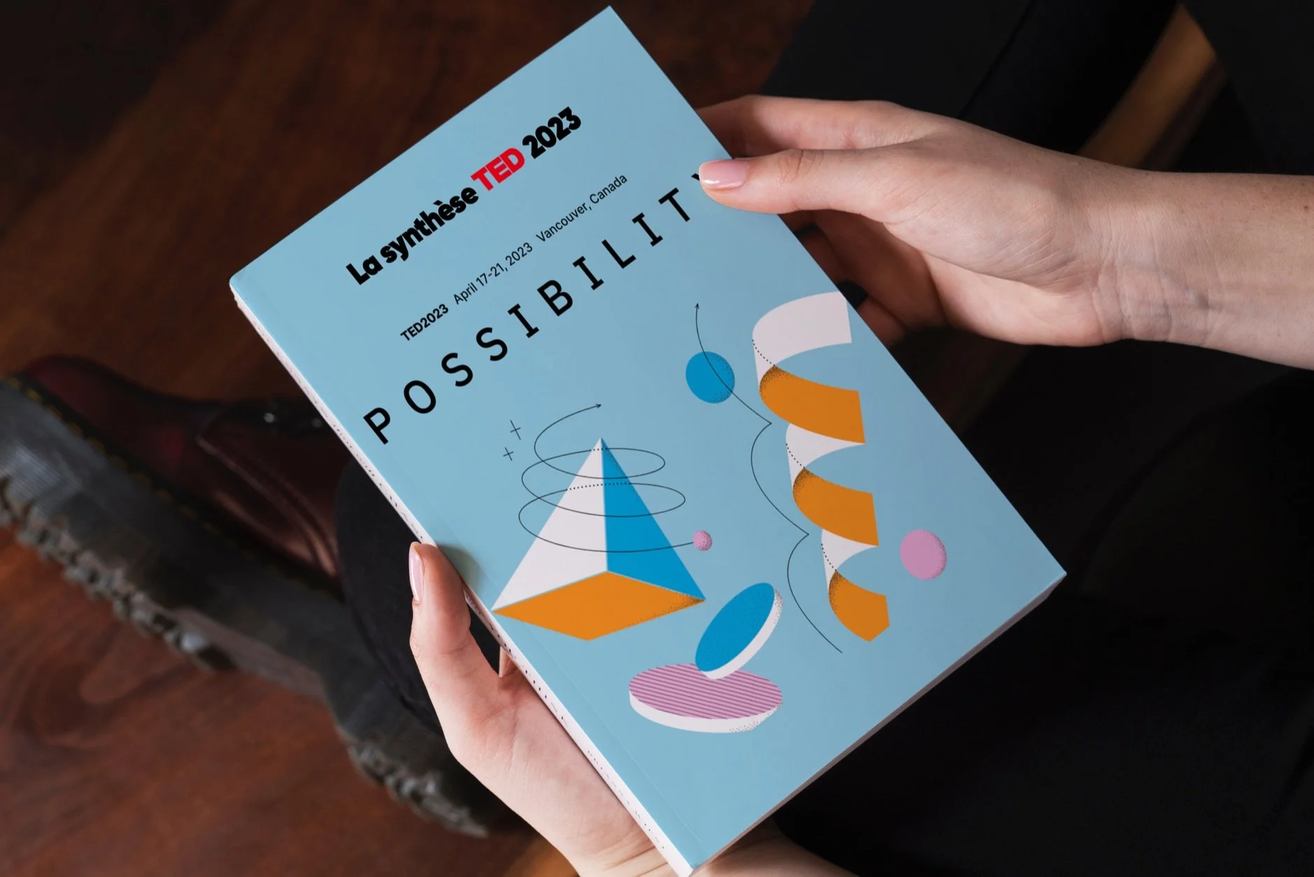 Livre avec titre 'La synthèse TED 2023, Possibilité', montrant dates du 17 au 21 avril 2023 à Vancouver, Canada, tenu par une personne en position assise.