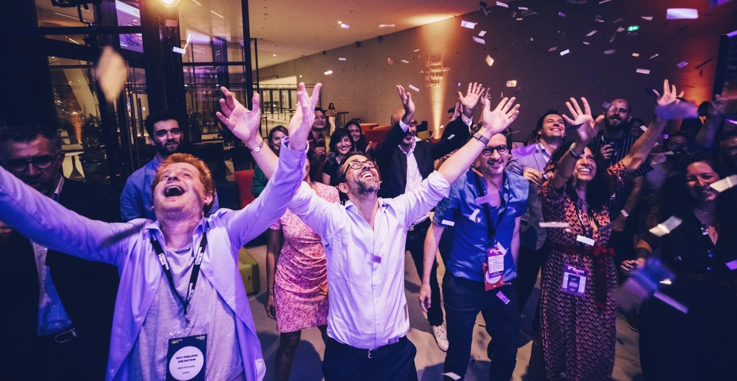 Groupe de personnes heureuses à une fête dans un centre de conférence, avec des expressions de joie et de célébration.