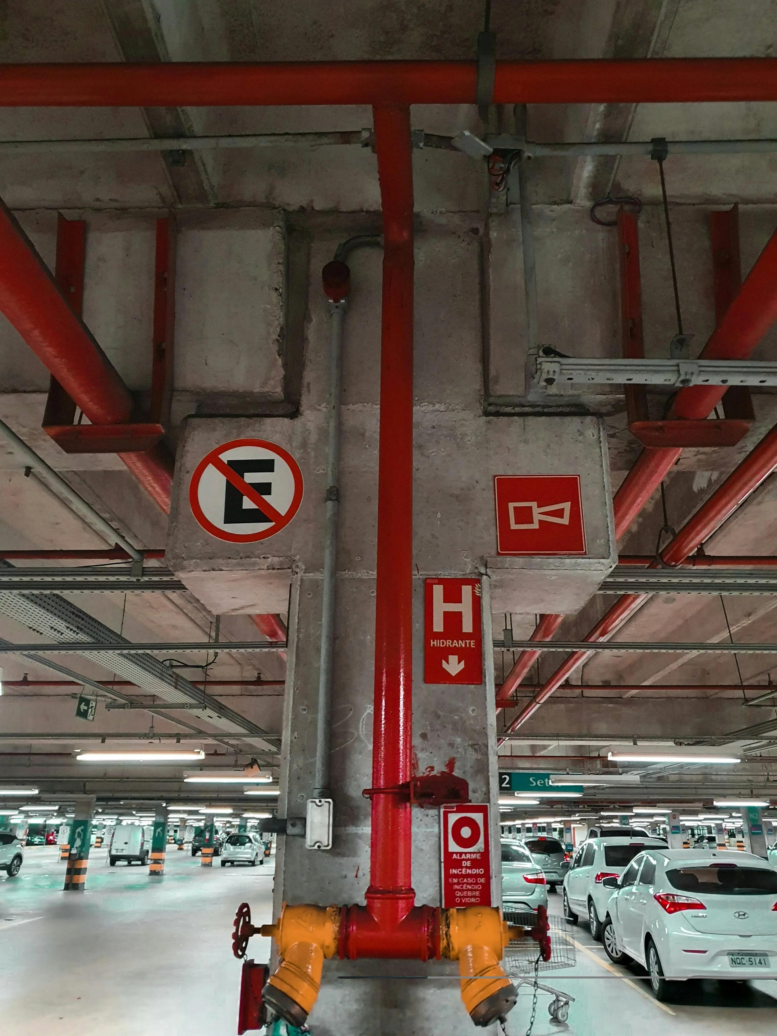 Fire safety equipment installed in an underground parking garage, including red pipes, a red alarm device, and safety signs.