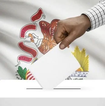 A person wearing a checked shirt is casting a ballot into a white ballot box in front of the Illinois state flag.