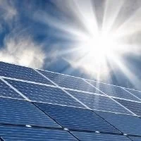 Close-up of solar panels reflecting sunlight against a blue sky with clouds.