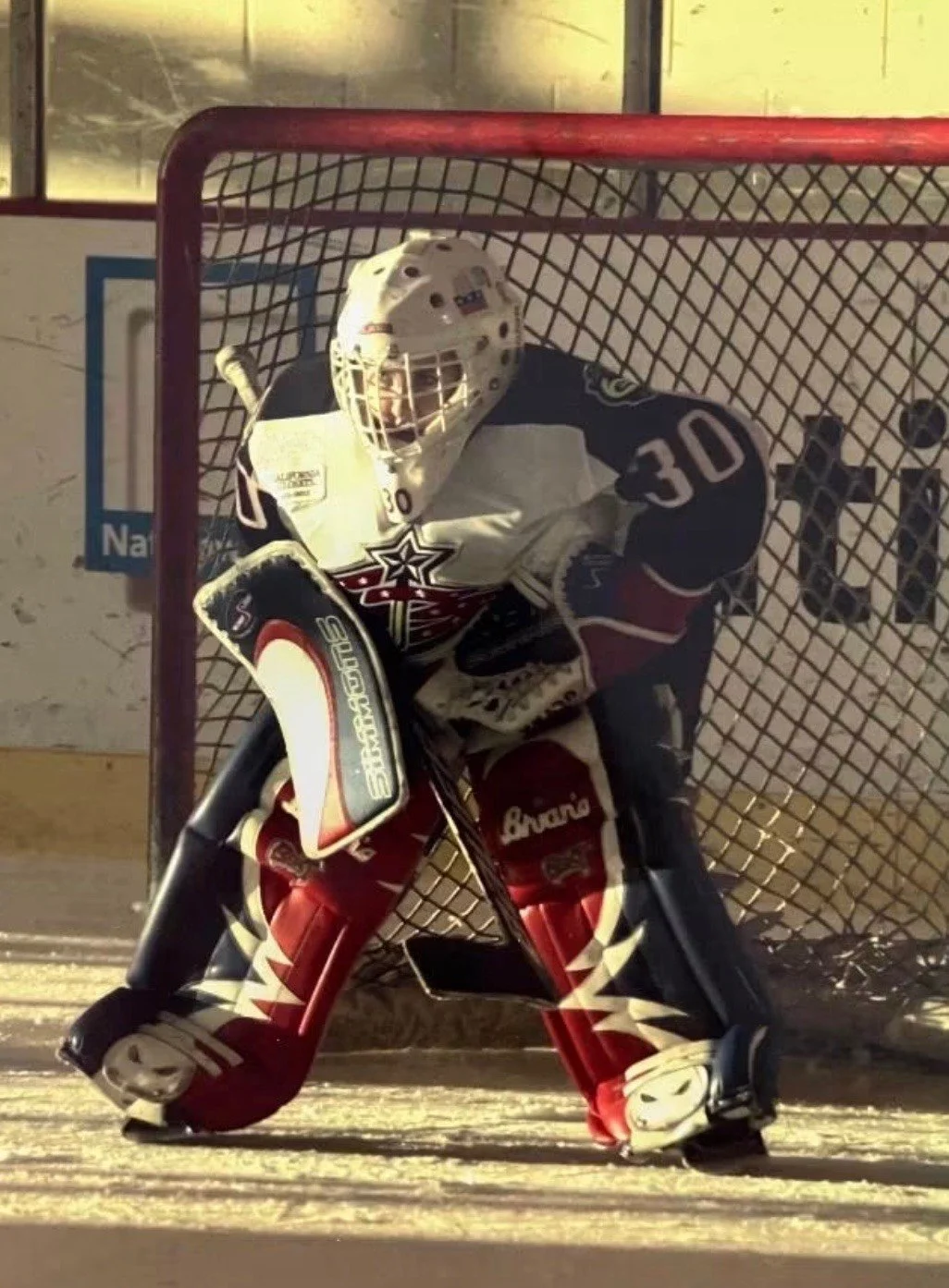 Hockey goalie in gear inside a net on an ice rink.