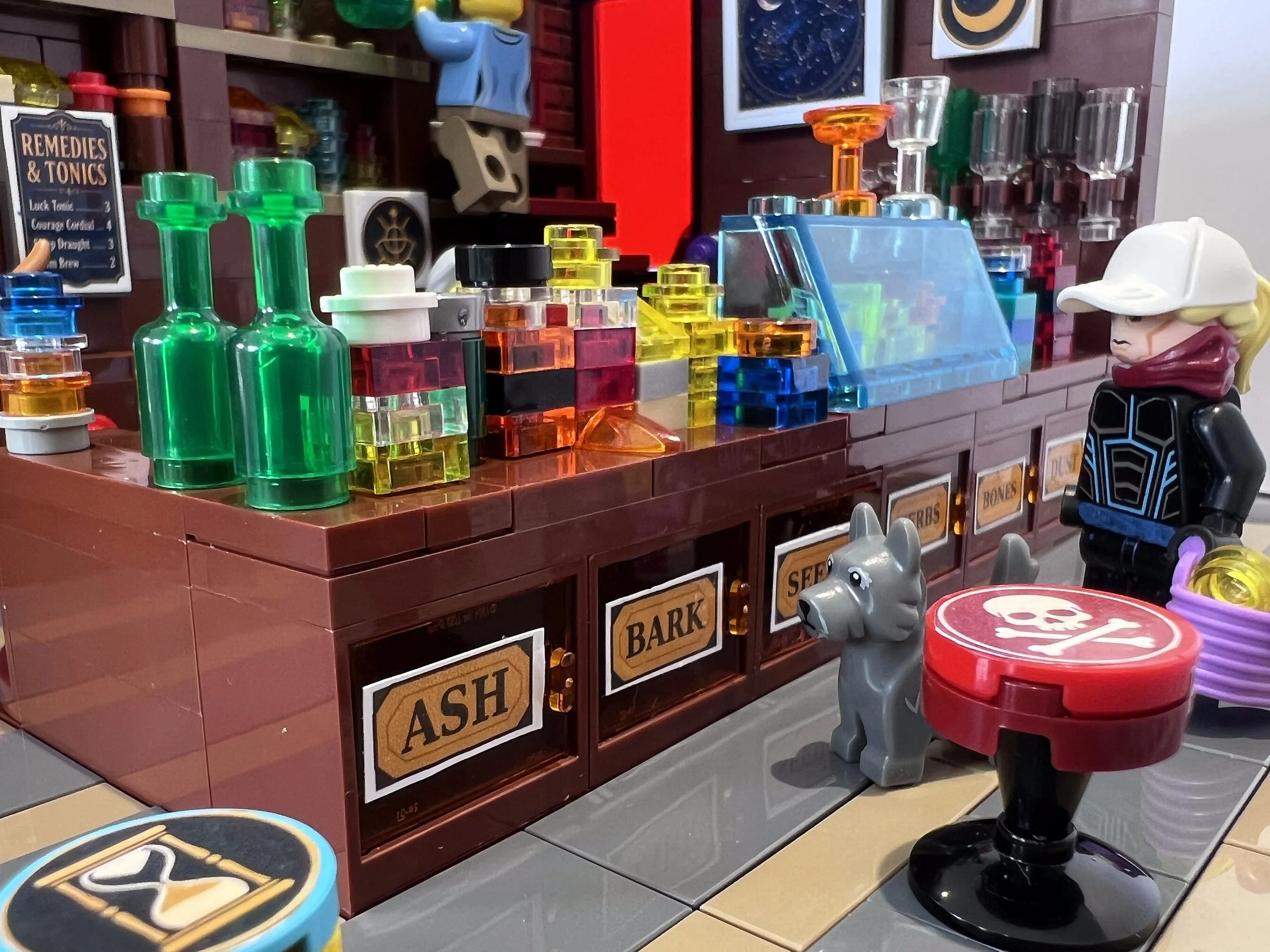 LEGO drawer plates on an apothecary counter reading Ash, Bark, Seeds, Herbs and Bones, with a customer waiting