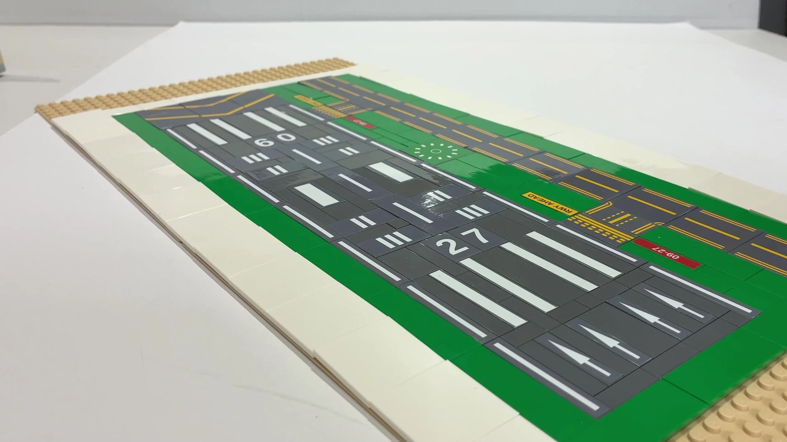 A LEGO airport runway and taxiway built from custom stickers on grey and green tiles