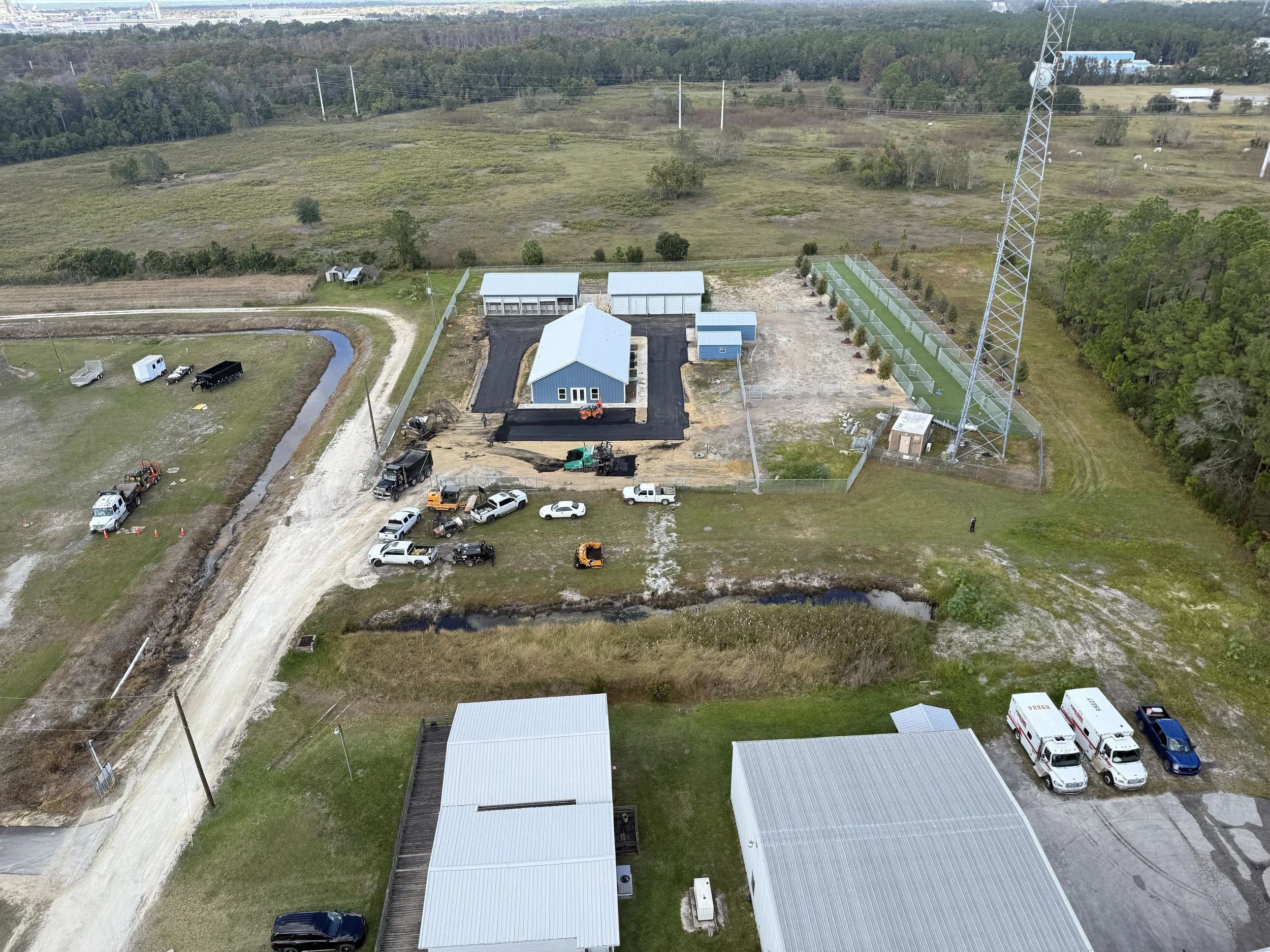 Aerial view of a construction site with a new parking lot, a building and surrounding equipment, vehicles, and landscape.