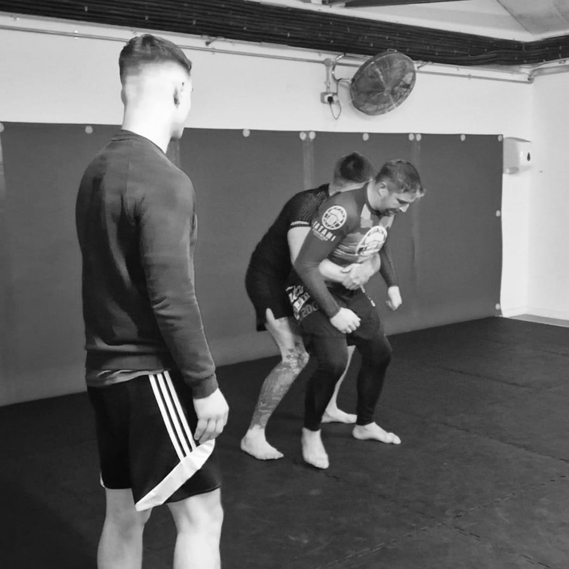 Three men practicing Brazilian Jiu-Jitsu on a mat in a training gym.