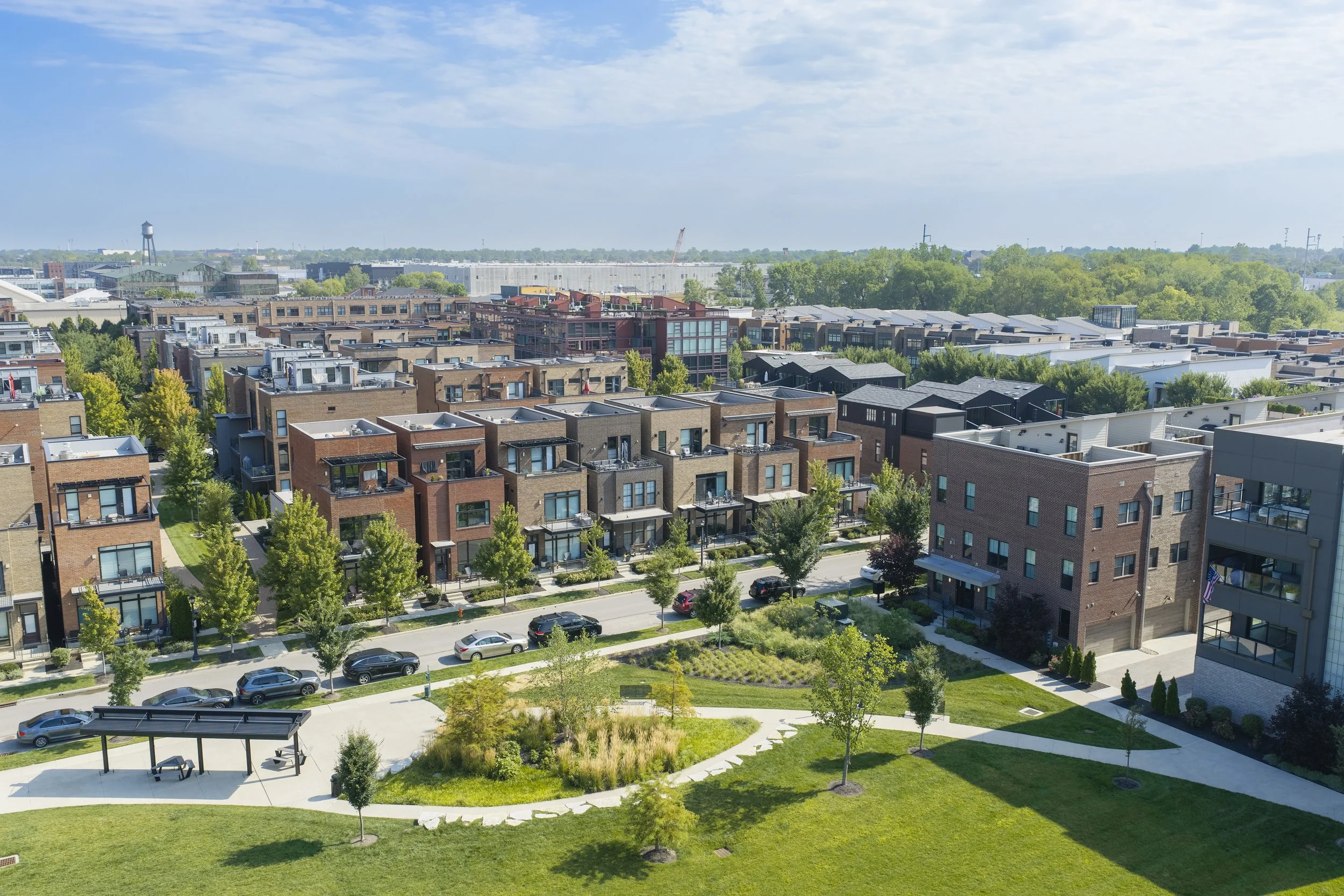View of a residential neighborhood with modern apartment buildings, green trees, and a park with pathways and benches.