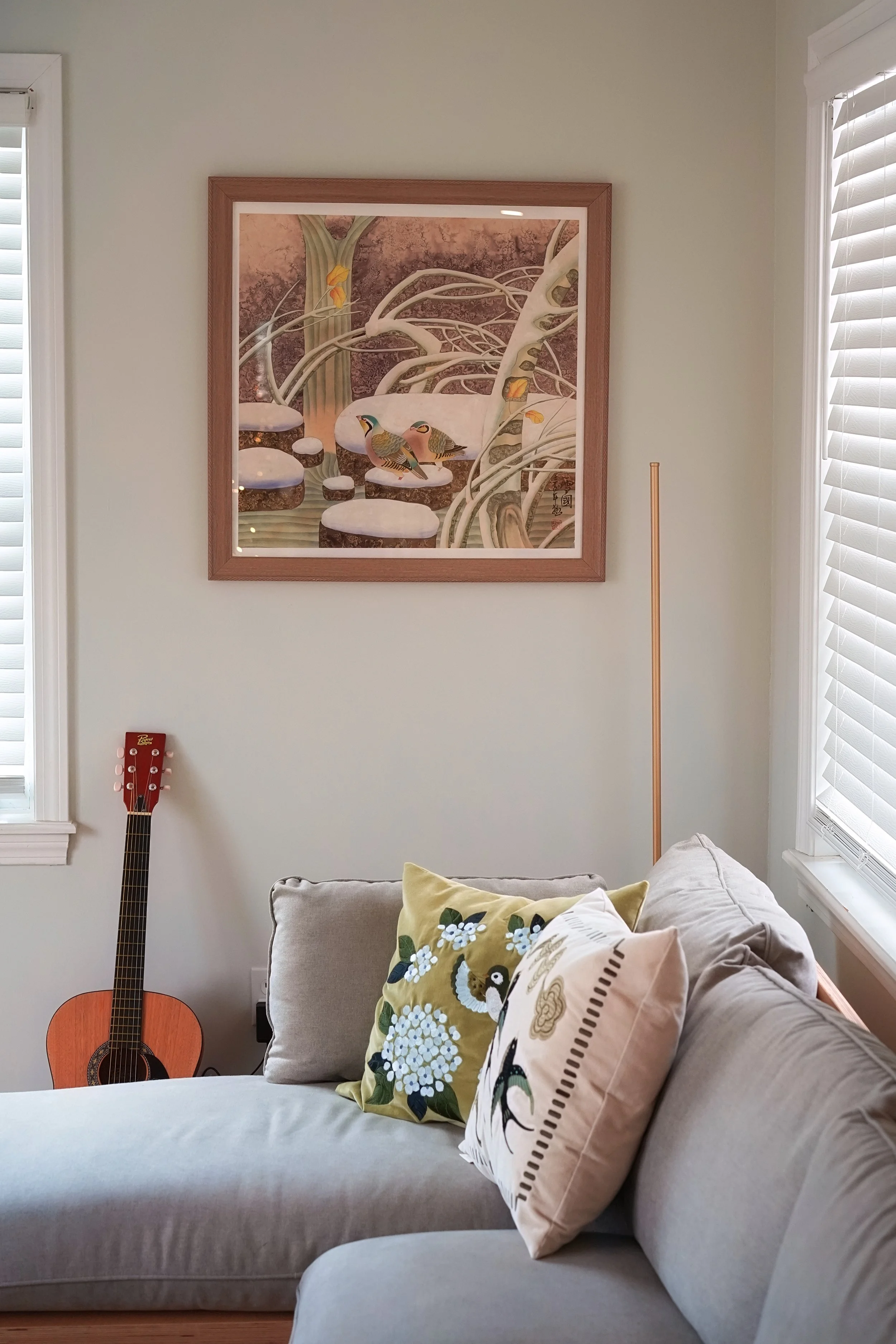 Living room wall with framed artwork, guitar, and couch with floral pillows.
