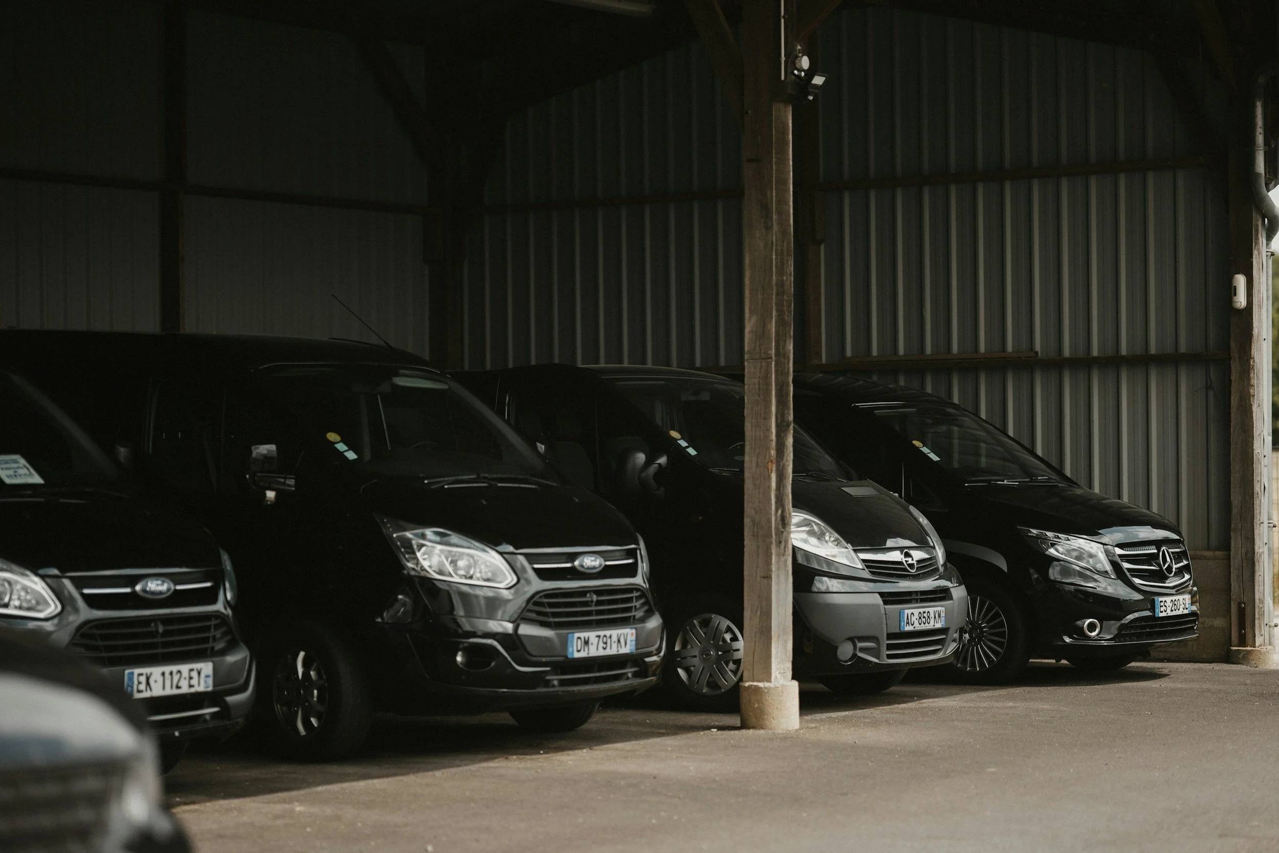 Photograph of a parked car garage with dark cars, metal siding, and wooden support beams.