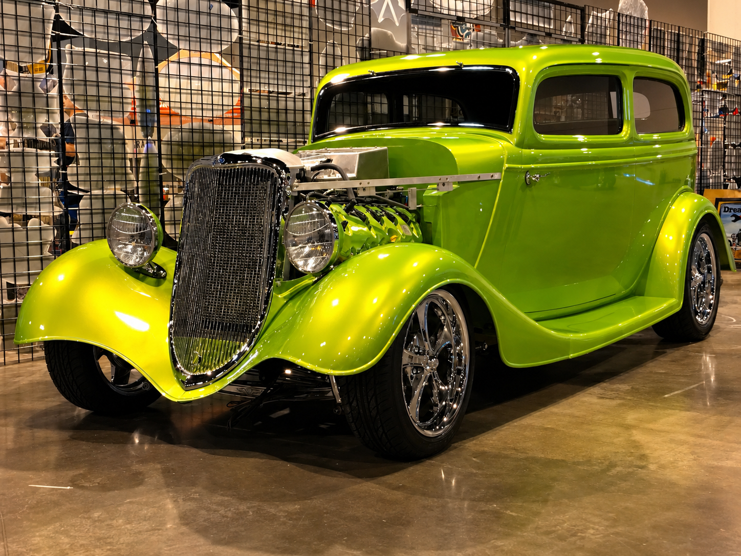 A bright green vintage car with a customized body and chrome wheels on display at an indoor auto exhibition.