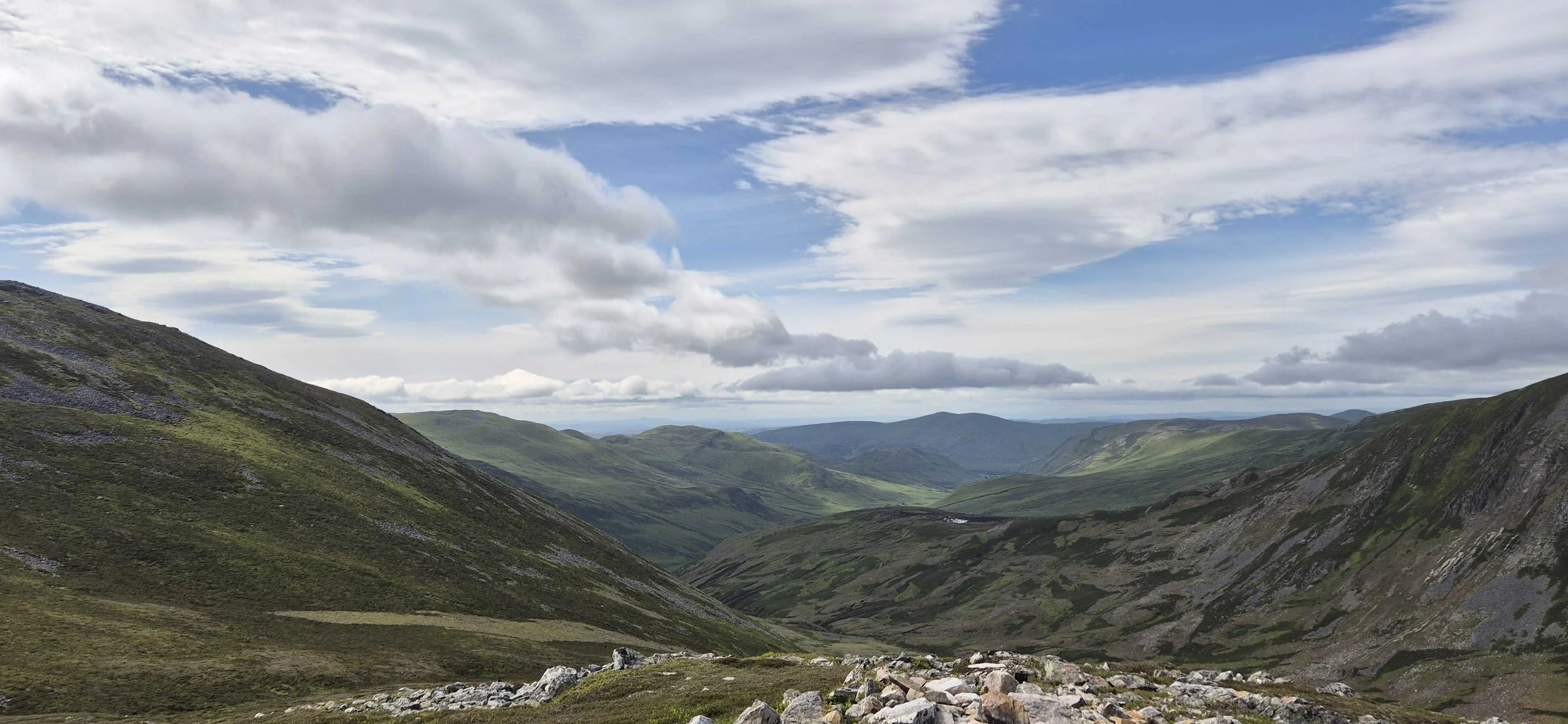 A scenic view of green, rolling hills and mountains under a partly cloudy sky.