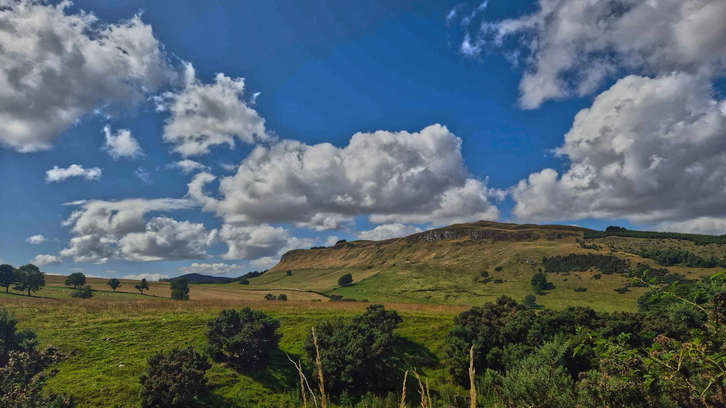 Dramatic wide-open hill landscape under massive, layered cloud formations in Scotland.