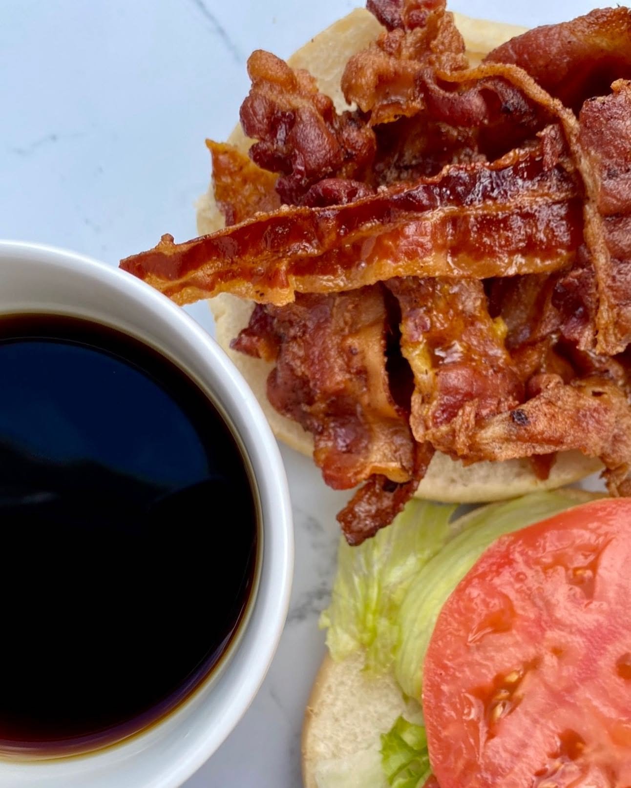 Breakfast sandwich with bacon, lettuce, tomato, and a side of black coffee.