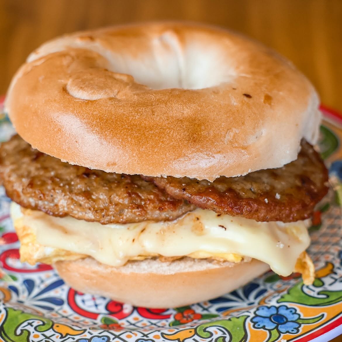 Breakfast bagel sandwich with sausage, fried egg, and cheese on a colorful plate.