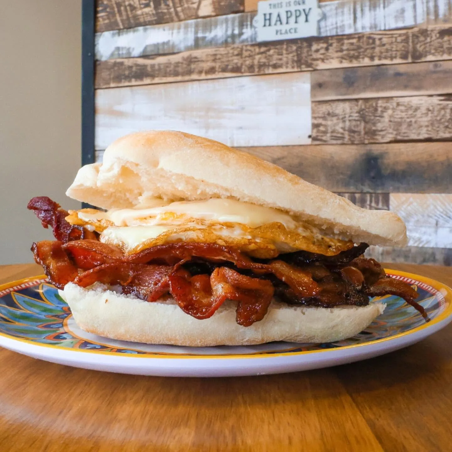 Close-up of a bacon, egg, and cheese breakfast sandwich on a colorful plate.