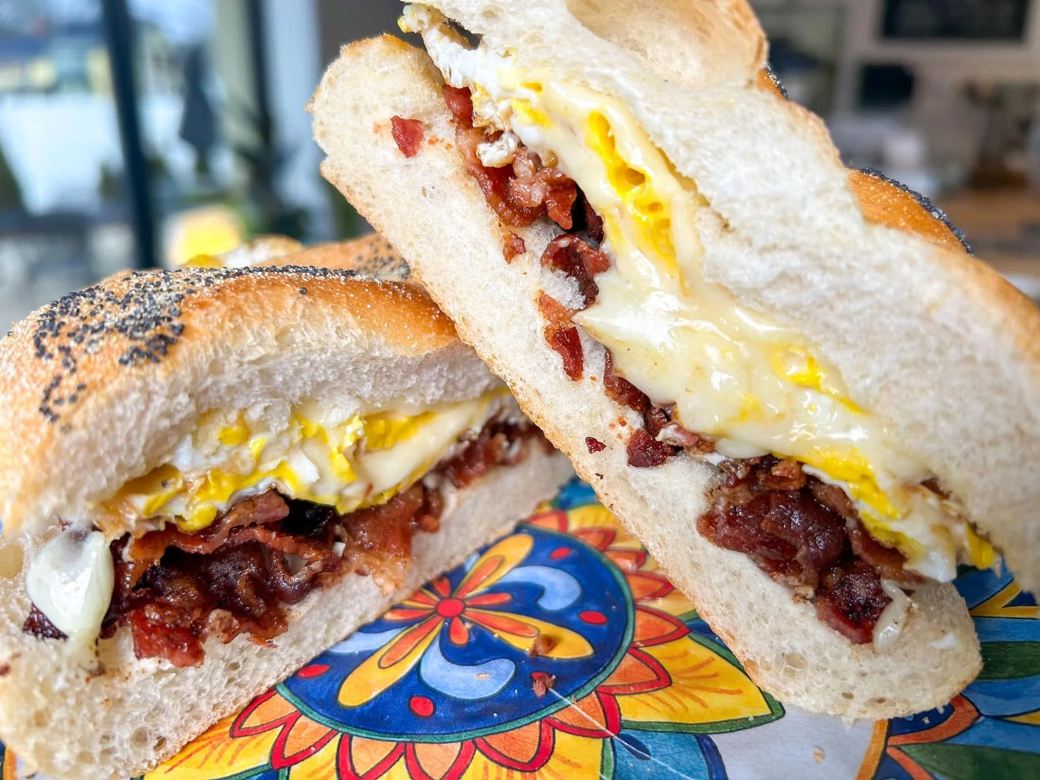 A sandwich with eggs, bacon, and cheese on toasted bread, placed on a colorful, patterned plate.