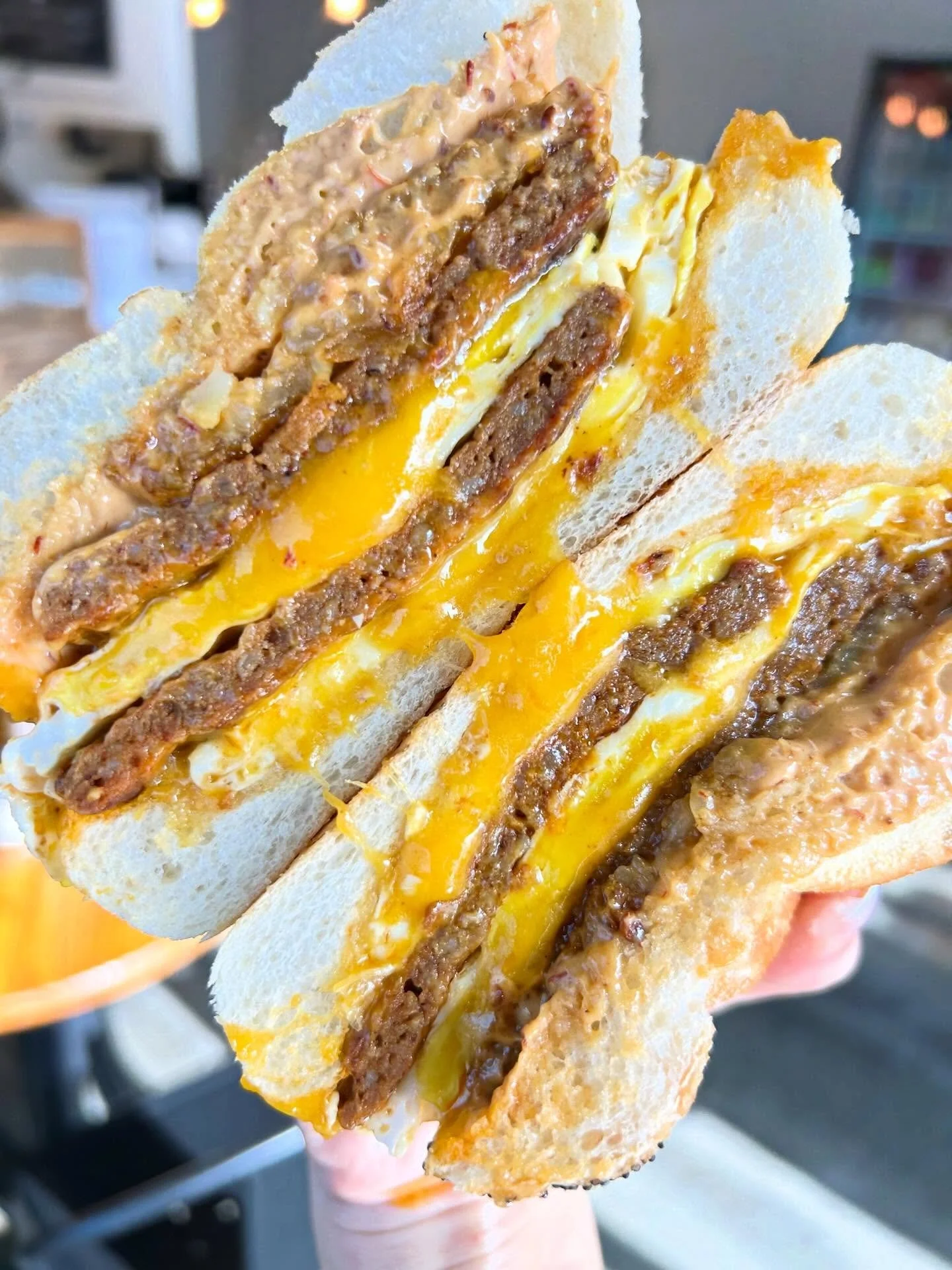 Close-up of a sandwich with chorizo patties, melted cheese, eggs, and chipotle sauce between slices of white bread.