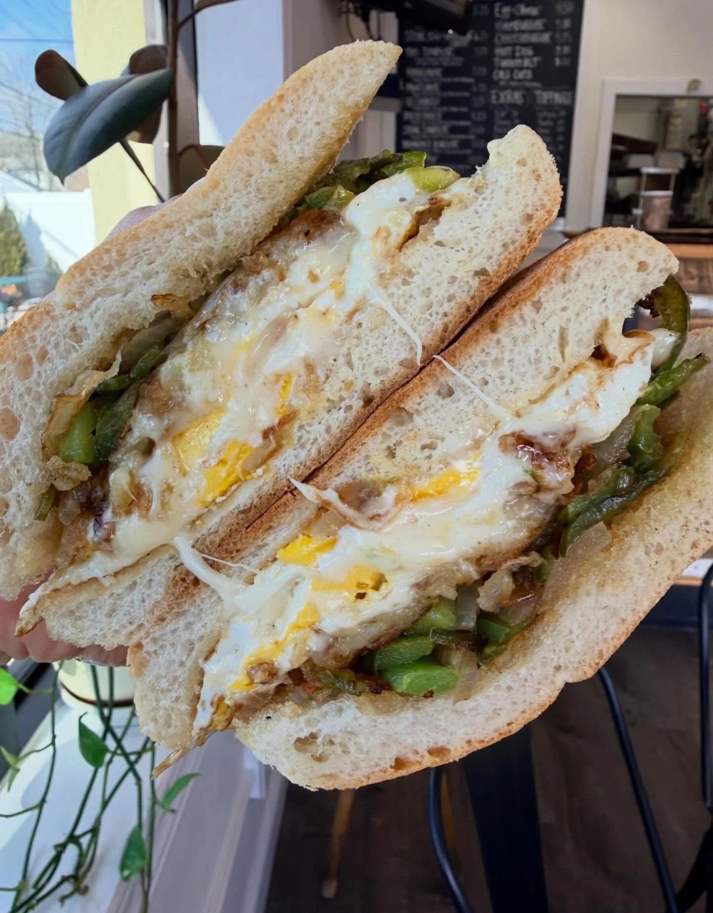 Close-up of a breakfast sandwich with fried eggs, green peppers, and bacon on toasted bread.