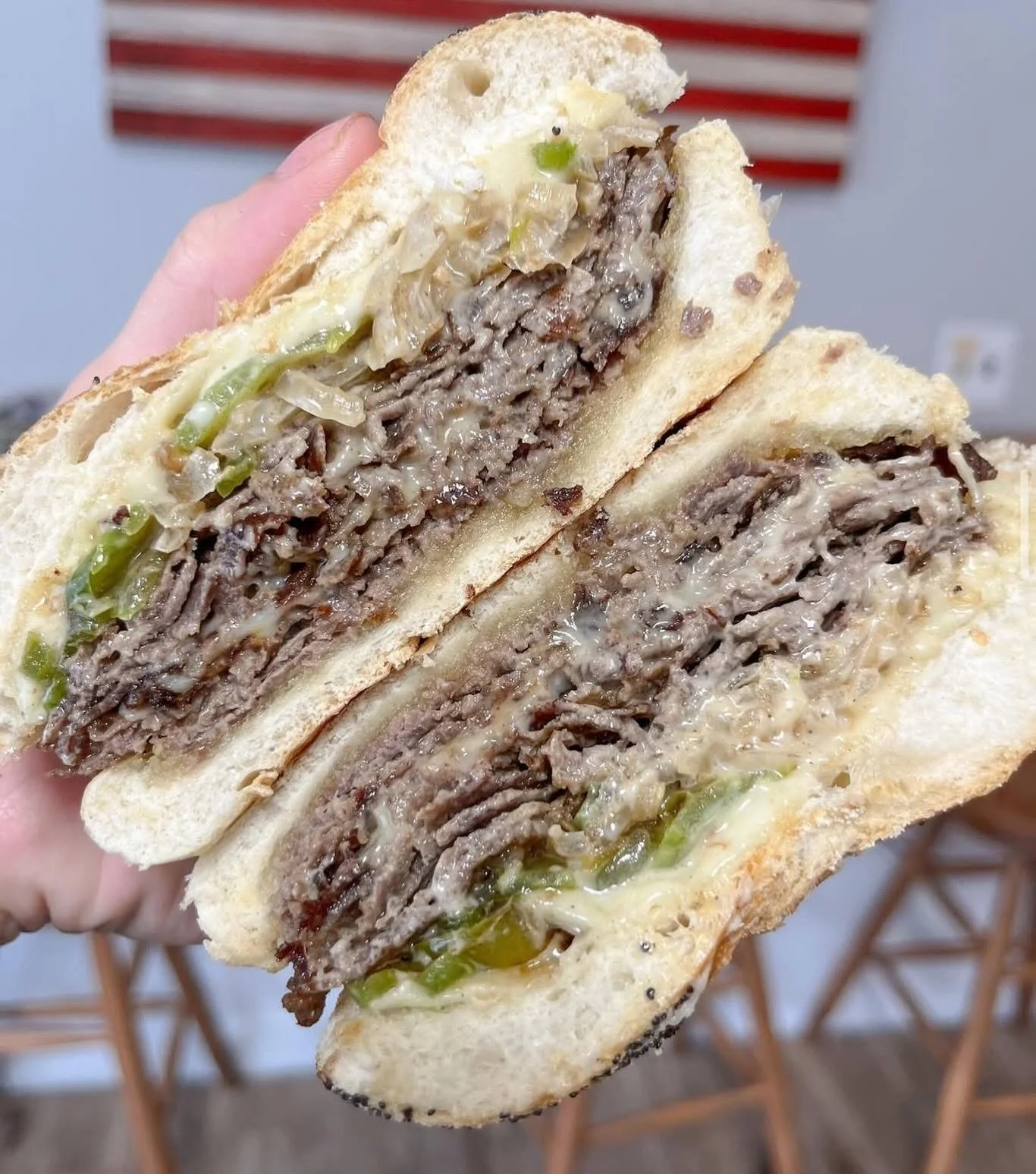 A close-up of a sliced beef sandwich with melted cheese, lettuce, and sauce on white bread.