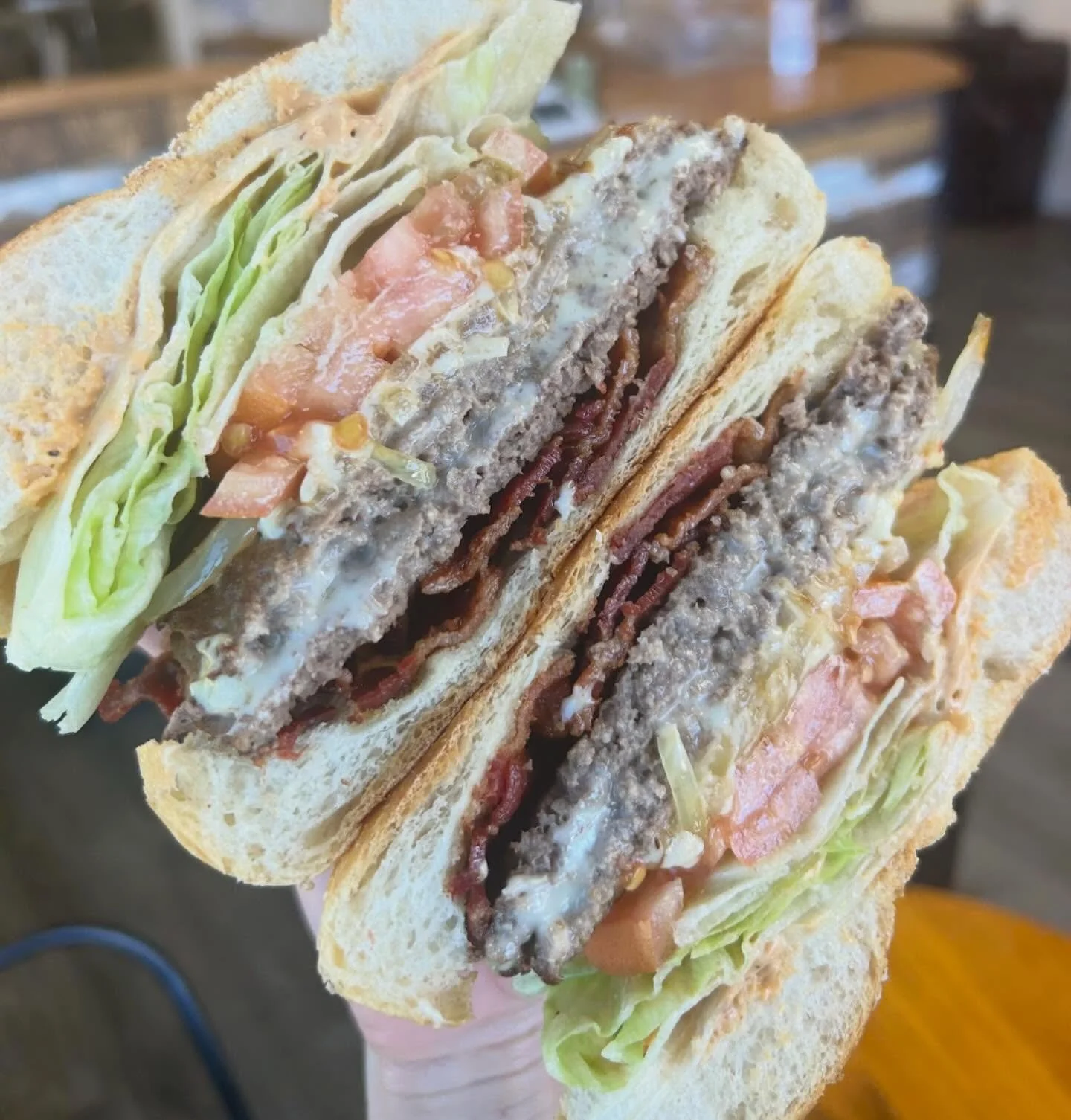 Close-up of three burger sandwiches with beef patties, lettuce, tomato, and various condiments, held together with wooden skewers.